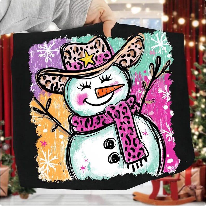 May include: Black tote bag with a whimsical snowman design. The snowman wears a leopard print cowboy hat and scarf, with a carrot nose. The background has colourful brushstrokes and snowflakes, creating a festive winter theme.