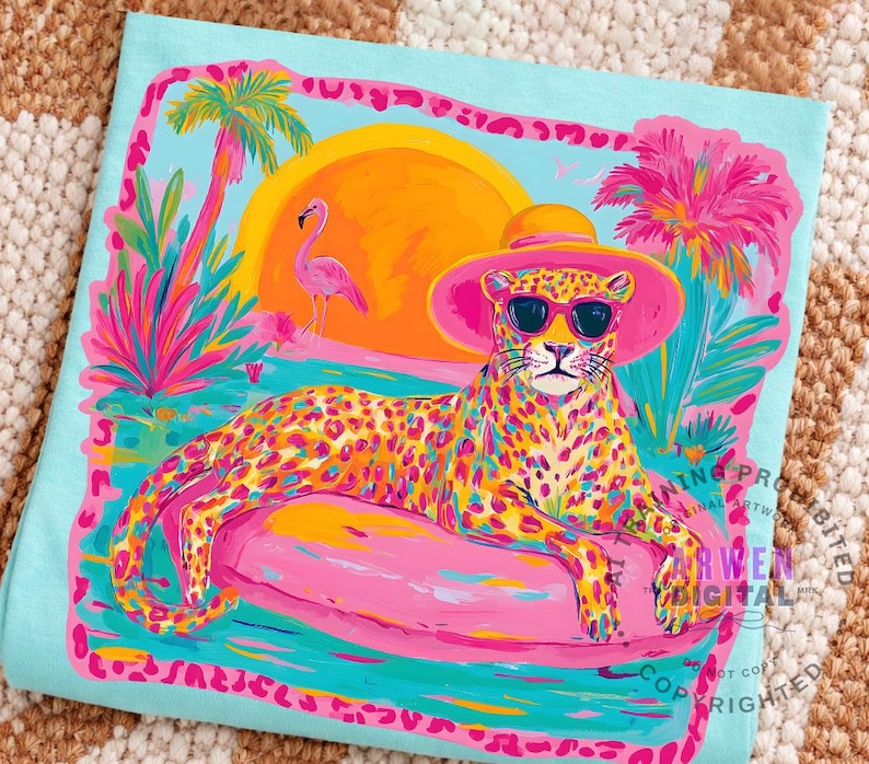 K&ouml;nnte beinhalten: Ein hellblaues T-Shirt mit einer farbenfrohen Illustration eines Leoparden mit Sonnenbrille und Hut, der auf einem rosa Schwimmer liegt. Das Design umfasst einen Sonnenuntergang, Palmen und einen Flamingo. Das Kunstwerk ist mit einem rosa Rahmen versehen.