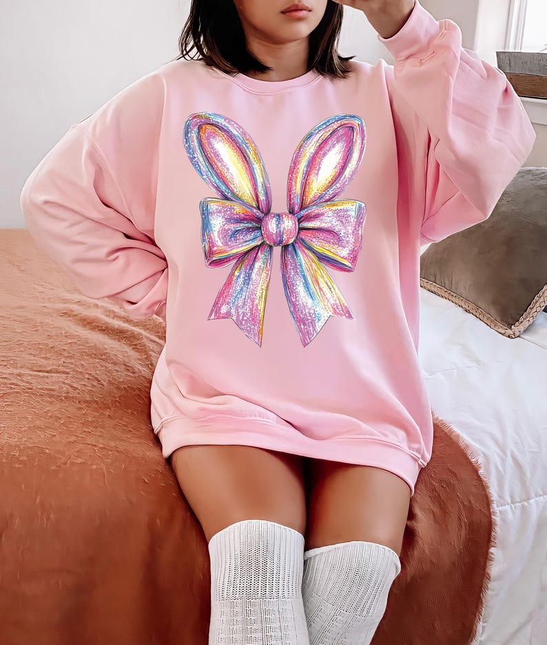 May include: A pink oversized sweatshirt with a large rainbow glitter bow graphic on the front.