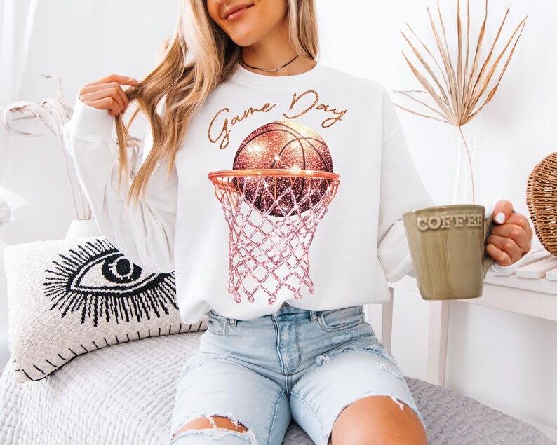 May include: White sweatshirt with a pink and gold basketball in a hoop and the text "Game Day".