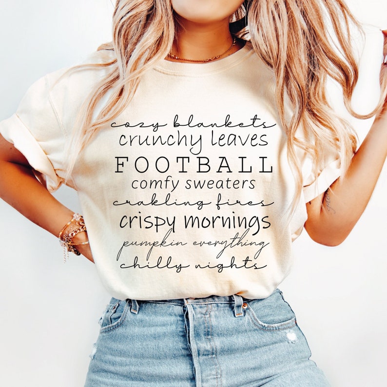 May include: Cream-colored t-shirt with black script text listing fall-themed words: cozy blankets, crunchy leaves, football, comfy sweaters, crackling fires, crispy mornings, pumpkin everything, and chilly nights.