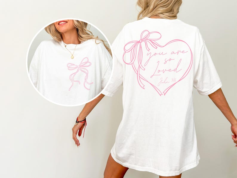 May include: White oversized t-shirt with a pink ribbon bow design on the front and a pink ribbon heart design on the back with the text "you are so loved John 3:16".