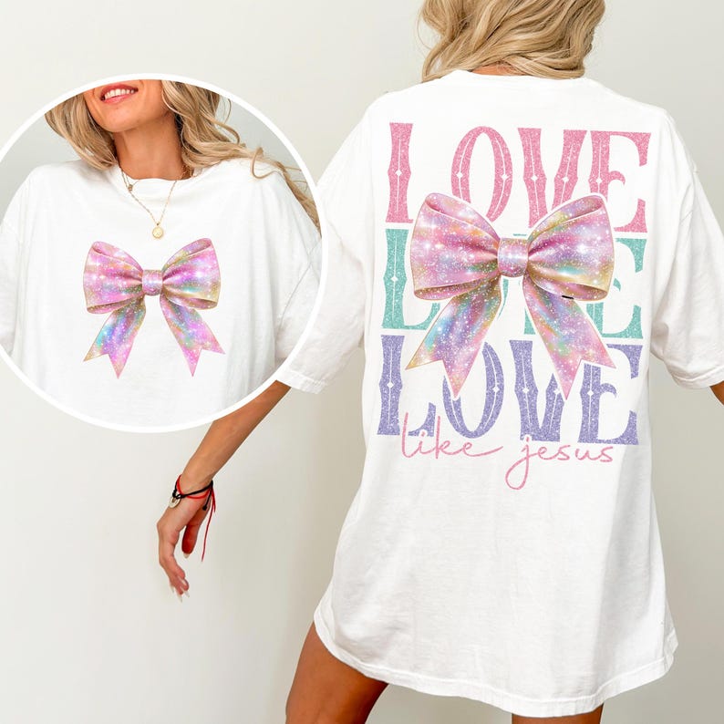 K&ouml;nnte beinhalten: Wei&szlig;es T-Shirt mit einer glitzernden rosa Schleife auf der Vorderseite und dem Text "LOVE LIKE LOVE like jesus" auf der R&uuml;ckseite.