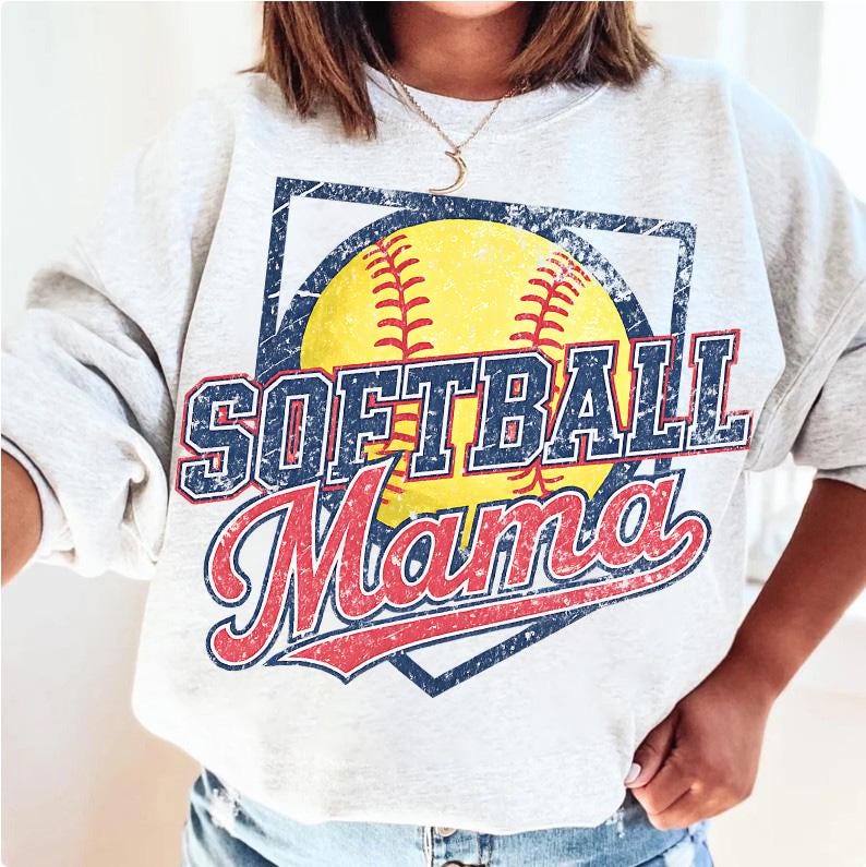 May include: A light gray sweatshirt featuring a distressed graphic of a yellow softball with red stitching, and the words "SOFTBALL Mama" in blue and red lettering. The design is set within a blue square.
