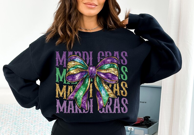 Puede incluir: Sudadera negra con un lazo brillante morado, verde y dorado y el texto "Mardi Gras" repetido tres veces.