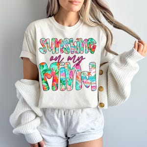 Pu&ograve; includere: Maglietta bianca con una grafica floreale che dice "Sunshine on my mind".