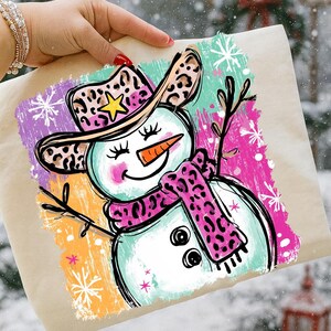 May include: A colourful illustration of a snowman wearing a leopard print cowboy hat and scarf. The snowman has a carrot nose, twig arms, and a smiling face. The background features colourful brushstrokes and snowflakes.