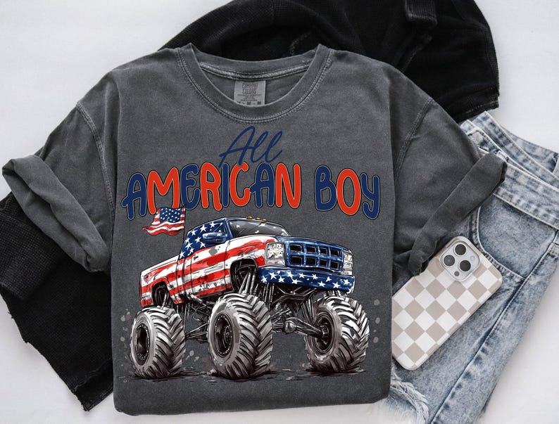 May include: Dark gray crew neck sweatshirt with the text "All AMERICAN BOY" in red and blue. The graphic features a monster truck with an American flag design. The shirt is folded with a pair of blue jeans and a phone case.