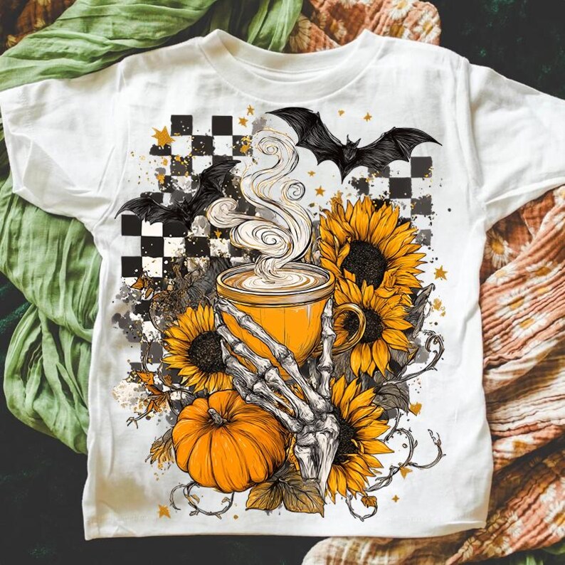 K&ouml;nnte beinhalten: Wei&szlig;es T-Shirt mit einem Halloween-Motiv. Die Grafik zeigt eine gelbe Kaffeetasse mit Dampf, Sonnenblumen, einen K&uuml;rbis und eine Skeletthand. Schwarze Flederm&auml;use und ein Schachbrettmuster vervollst&auml;ndigen das Design.