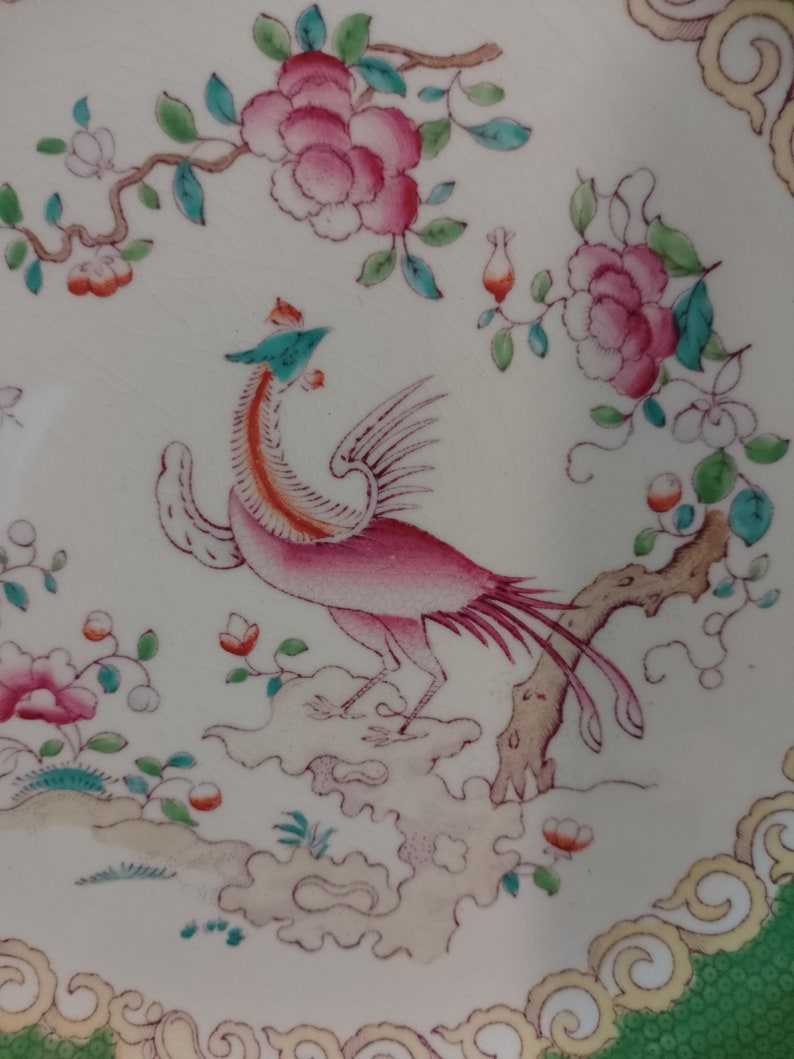 May include: A vintage ceramic plate with a pink and green floral design and a pink and red bird perched on a branch. The plate has a green and gold border.