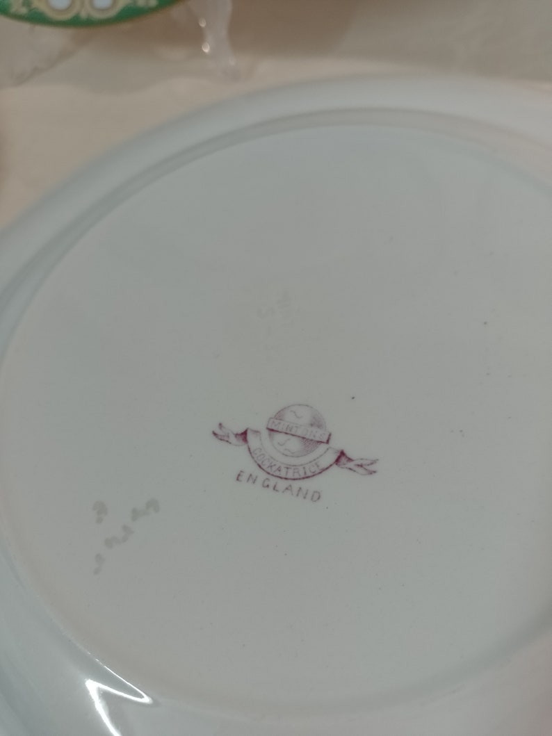 May include: A white ceramic plate with a pink and white logo that reads "Mintons Oakatrice England".