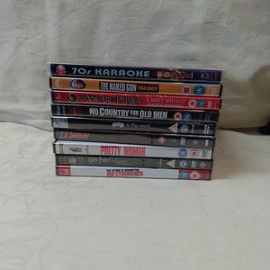 May include: A stack of nine DVDs featuring various movies, including "The Naked Gun Trilogy", "No Country for Old Men", and "Pretty Woman".