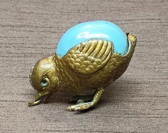 以下が含まれることがあります： 背中 に 青い エナメル の 卵 を 乗せ た 金 の 鳥 の 置物 です 。 鳥 は 屈ん だ 姿勢 で 頭 を 下 に 向け て い ます 。 置物 は うろこ と 羽根 で 細かく 作ら れ て い ます 。