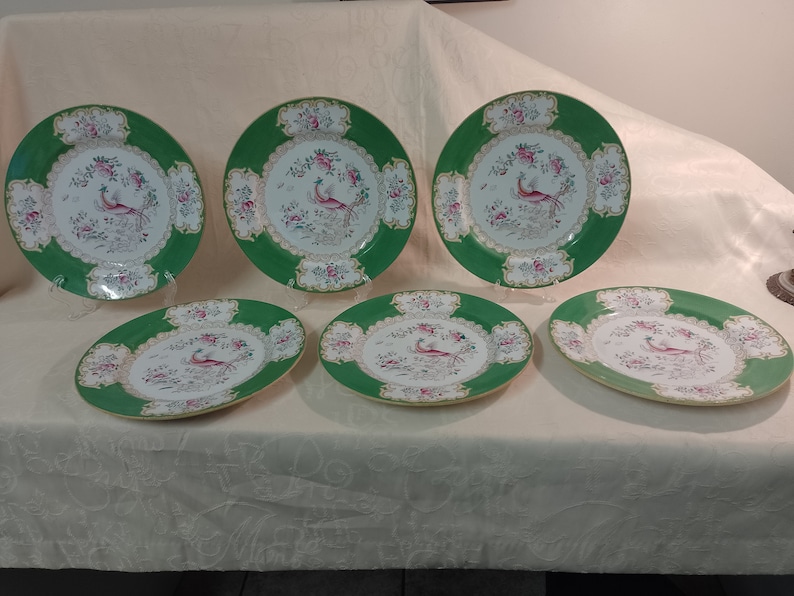 May include: Set of six green and white porcelain dinner plates with a gold trim. Each plate features a delicate floral design and a colorful bird in the center.