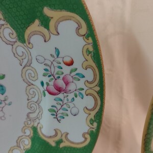 May include: A green and white ceramic plate with a gold rim and floral design. The plate has a textured green surface and a white center with a floral pattern in pink, red, and green.