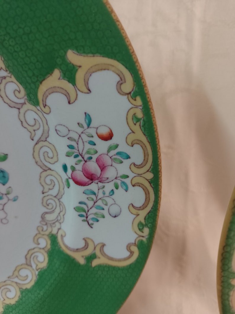 May include: A green and white ceramic plate with a gold rim and floral design. The plate has a textured green surface and a white center with a floral pattern in pink, red, and green.