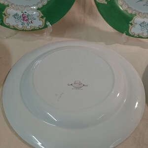 May include: A white ceramic plate with a green rim and floral pattern. The back of the plate has a stamp that reads "Royal Doulton England".