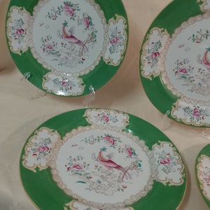 May include: Four green and white porcelain plates with a gold trim and a pink and white bird design.