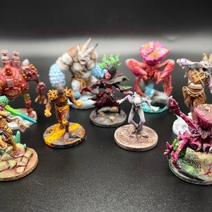 May include: A collection of eight hand-painted miniature figures, each on a circular base. The figures include a humanoid with a sword, a creature with a large head, a creature with a crab-like body, a humanoid with a staff, a humanoid with a horned helmet, a humanoid with a large head, a humanoid with a staff, and a creature with a large head.