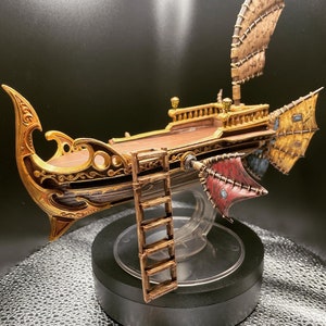 May include: A detailed miniature model of a ship with intricate gold and brown details. The ship has a large sail and a ladder on the side. The ship is displayed on a black base with a clear plastic dome.