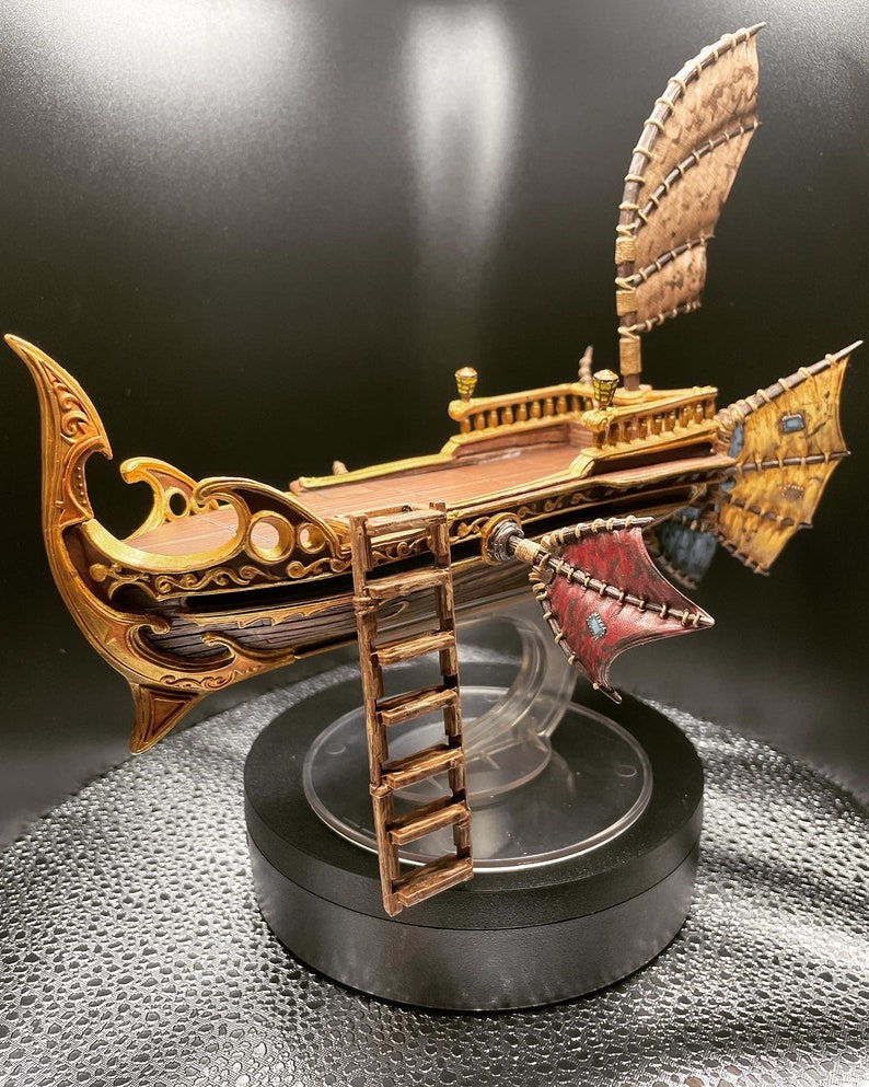May include: A detailed miniature model of a ship with intricate gold and brown details. The ship has a large sail and a ladder on the side. The ship is displayed on a black base with a clear plastic dome.