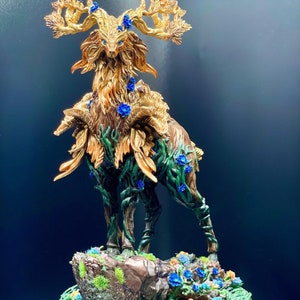 May include: A golden deer statue with antlers made of branches and leaves. The deer is covered in vines and blue flowers. The statue is standing on a rock base with green moss and flowers.