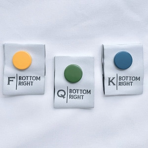Puede incluir: Tres etiquetas de tela con círculos de diferentes colores y el texto "BOTTOM RIGHT" en cada una. Las etiquetas están etiquetadas con las letras "F", "Q" y "K".