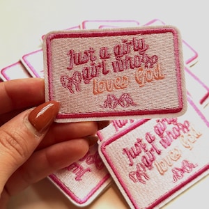May include: Pink and white embroidered patch with the text "Just a girly girl who loves God" and a pink moustache.
