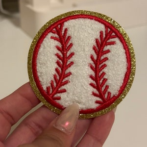 May include: A white baseball patch with red stitching and a gold glitter border.
