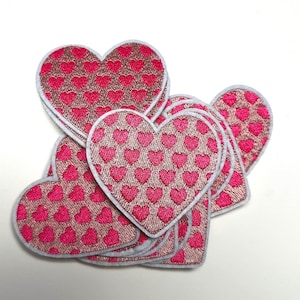 Op de afbeelding: Een stapel roze hartvormige patches met een witte rand. Elk hart is bedekt met een patroon van kleinere roze harten.