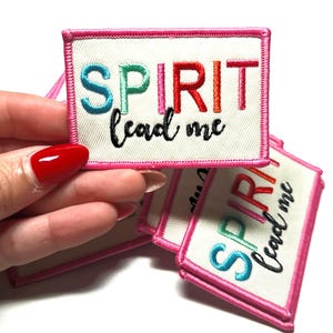 May include: A set of four embroidered iron-on patches with a white background and pink border. The patches feature the text "SPIRIT lead me" in colorful lettering.