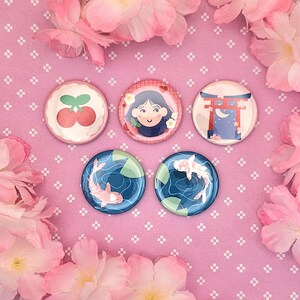 Peut inclure: Cinq badges ronds illustrés : une paire de cerises rouges, une personne souriante aux cheveux noirs avec des fleurs, un torii rouge de nuit, et deux badges représentant des carpes koï blanches et roses nageant dans une eau bleue.