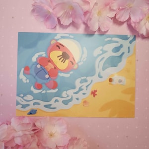 Op de afbeelding: Een cartoonillustratie van een rode en gele beer die een blauw-witte matrozenoutfit draagt ​​en op zijn rug drijft in blauw water met witte golven. De beer glimlacht en heeft zijn ogen dicht. De achtergrond is een geel strand met een bruine fles en een rode zeester.