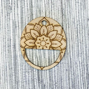 Może przedstawiać: Drewniana ozdoba w kształcie jajka z wzorem mandali w kolorze brązowym i beżowym. Ozdoba ma otwór na górze do zawieszenia.