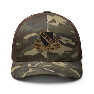 Puede incluir: Gorra de béisbol de camuflaje con una parte trasera de malla marrón y una visera curva. La parte delantera presenta un emblema bordado con el texto "FURY FROM THE SKY" en una pancarta. El patrón de la gorra incluye tonos de verde, marrón y beige.