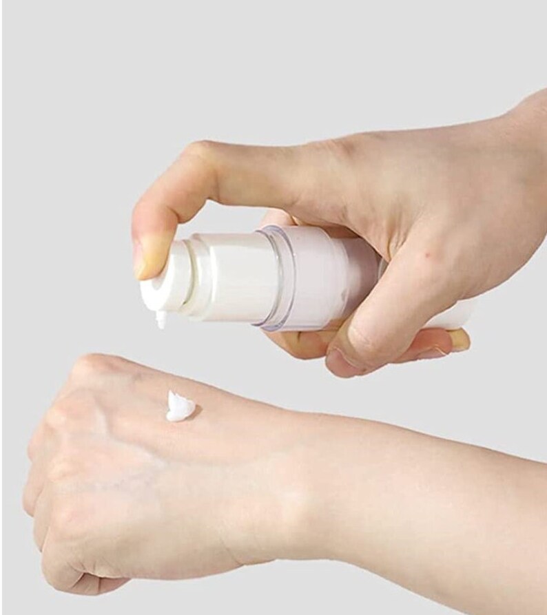 Puede incluir: Una botella de pl&aacute;stico blanca con una bomba y un cuerpo transparente que dispensa una crema blanca en la mano de una persona.