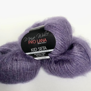 May include: Two skeins of purple mohair yarn labelled "Meine Wolle Pro Lana Kid Seta" with the text "70% Mohair/mohair 25g 210m".