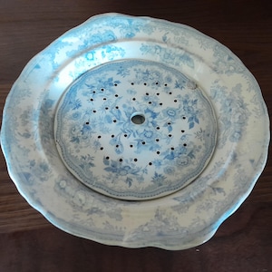 Op de afbeelding: Een tweedelige keramische vergiet met blauw-witte bloempatronen. De vergiet heeft een geperforeerd midden en zit in een bijpassende ondiepe kom. Het ontwerp heeft een delicaat bloemmotief.