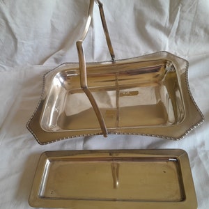 Peut inclure: Un plateau de service en argent avec une poignée et un plateau plus petit assorti. Le plateau a un bord perlé et une forme rectangulaire.