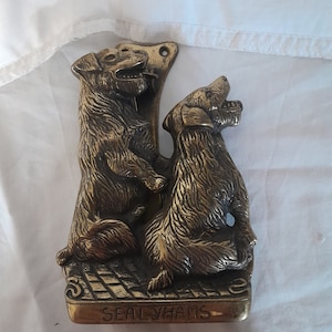 Op de afbeelding: Een messing deurklopper met twee Sealyham Terriers, een staat op zijn achterpoten en de ander zit. De klopper is gemonteerd op een rechthoekige basis met de inscriptie "Sealyhams".