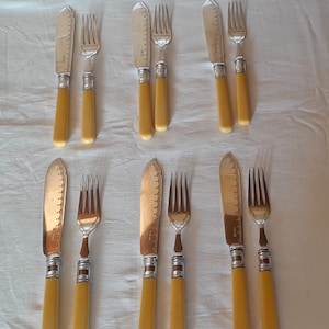 May include: Set of six silver-plated knives and forks with ivory-colored handles. The knives have serrated blades and the forks have four tines.