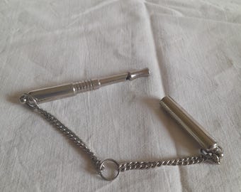 May include: A silver dog whistle with a chain attached. The whistle is in two pieces, one is a tube and the other is a mouthpiece.