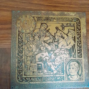 Puede incluir: Placa metálica cuadrada envejecida con un relieve detallado que representa una reunión, una esfera de reloj y el texto "THE JOLLY BEGGARS" y "BURNS". La placa tiene un borde decorativo y un retrato.