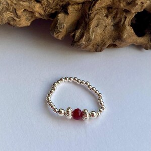 May include: A silver beaded ring with a single red gemstone bead.