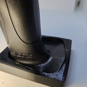 May include: Black plastic base with a textured surface and the word "SLTZ" printed on it. A black plastic handle is attached to the base.