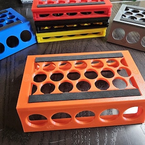 May include: An orange storage container with circular holes, and black pads. Other containers in blue, red, black, yellow, and grey are visible. These containers are designed to hold small cylindrical objects. The containers are likely used for organizing items.