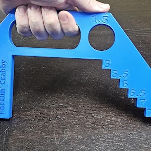 May include: A bright blue tool with a handle and a series of stepped measurements from 5 to 8, with a 1.5-inch circle. The text "Pheeelin' Crabby" is printed on the side. The tool is held by a hand.