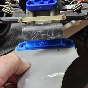 Może przedstawiać: Zbliżenie na niebiesko-czarny podwozie samochodu RC Traxxas z białym plastikowym ramieniem zawieszenia i czarnym i srebrnym amortyzatorem. Podwozie jest wykonane z plastiku i ma niebiesko-czarną kolorystykę. Ramię zawieszenia jest wykonane z białego plastiku i ma czarny plastikowy amortyzator przymocowany do niego. Amortyzator jest wykonany z czarnego plastiku i ma srebrną sprężynę przymocowaną do niego.