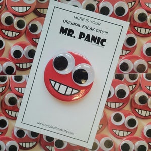 May include: Red button with googly eyes and a smiling mouth. The button says "Here is your Original Freak City™ Mr. Panic" with a copyright symbol and the year 2022. The button is surrounded by other red buttons with googly eyes.