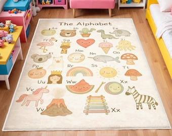 Op de afbeelding: Beige kinderkleed met het alfabet en kleurrijke illustraties van dieren en objecten. Het kleed heeft een witte rand en de woorden "The Alphabet" bovenaan.
